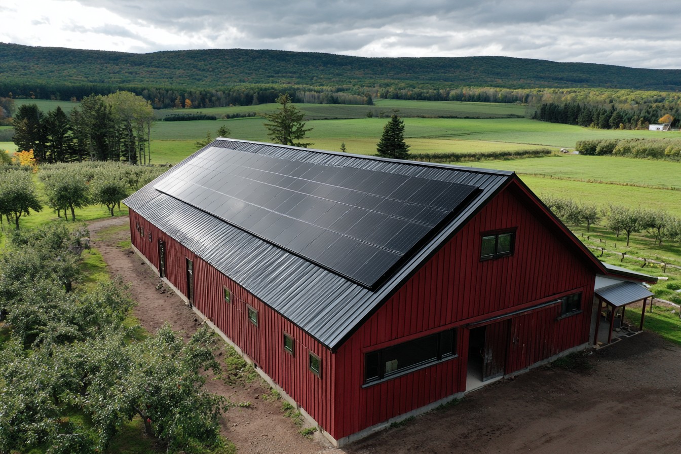 Large red barn with all-black solar-covered roof in Annapolis Valley farmland